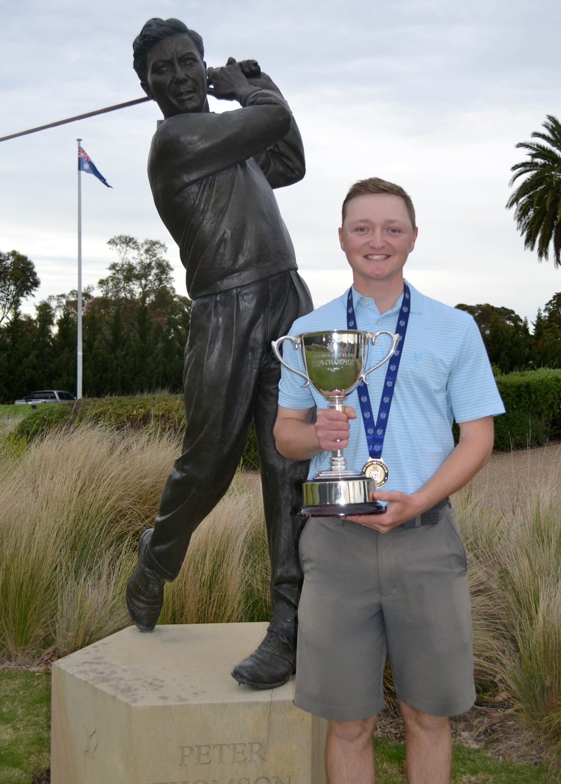 A player with a trophy beside a golfer statue